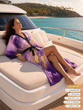 Load image into Gallery viewer, Woman lounging on a yacht sunbed in the Lilac Sanctum silk peignoir, ombré cuff and hem style with black trim and tie