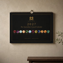 Load image into Gallery viewer, The Australian Crystal Calendar 2027 by Majestical hanging on a wall, black and gold cover with twelve birthstone medallions

