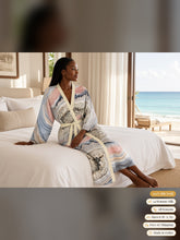 Load image into Gallery viewer, Woman sitting on the edge of a white villa bed in the Geode Gate silk peignoir, classic style with ivory trim and tie
